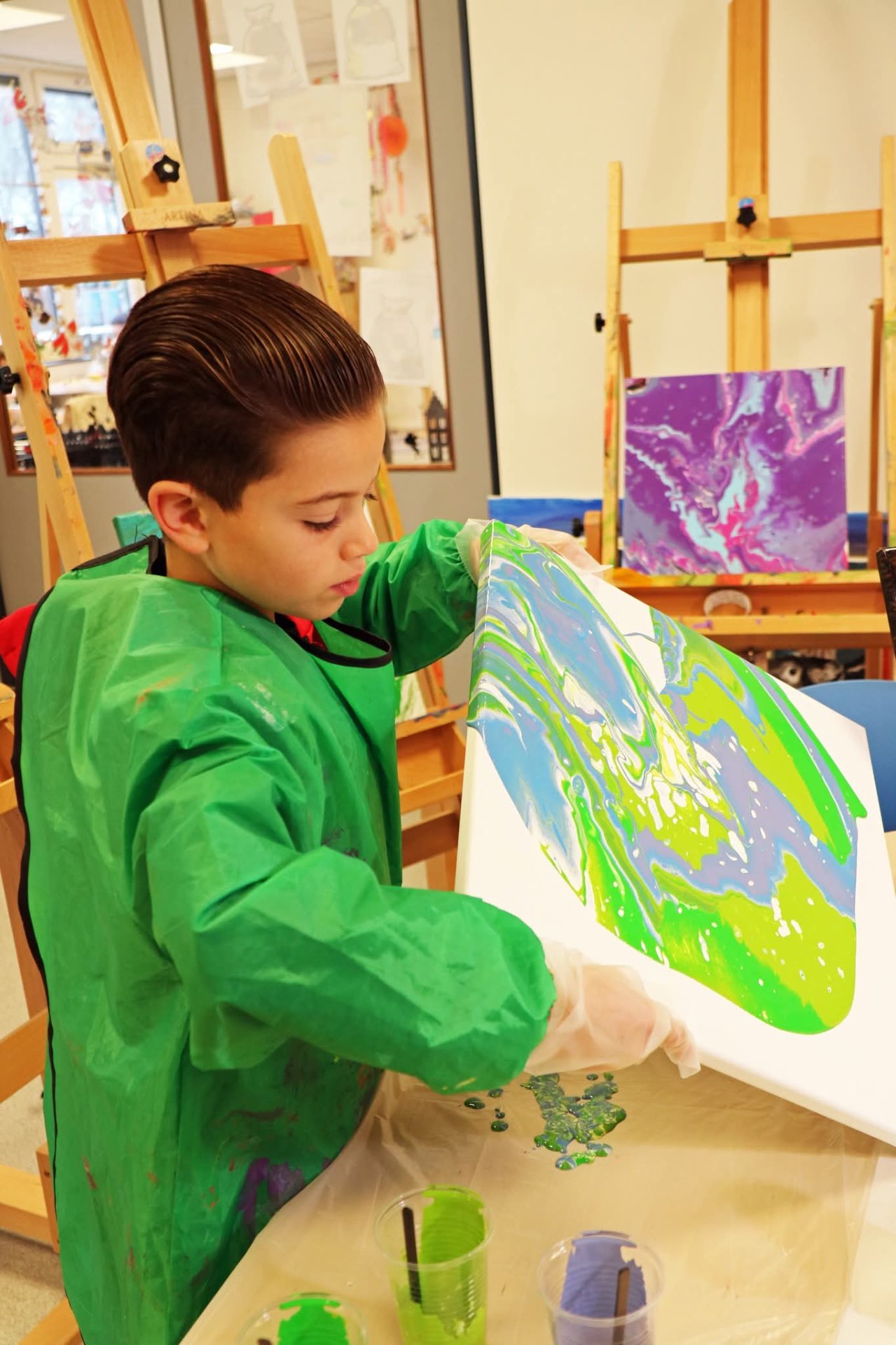 Jongen kantelt zijn canvas met blauw en groen pouring